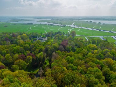 Uçsuz bucaksız yeşil tarlaları, dolambaçlı su yolları ve Hollanda 'nın düz kırsalında parçalı bulutlu bir gökyüzünün altında uzanan bir nehirle çevrili tarihi bir şatonun havadan görünüşü..