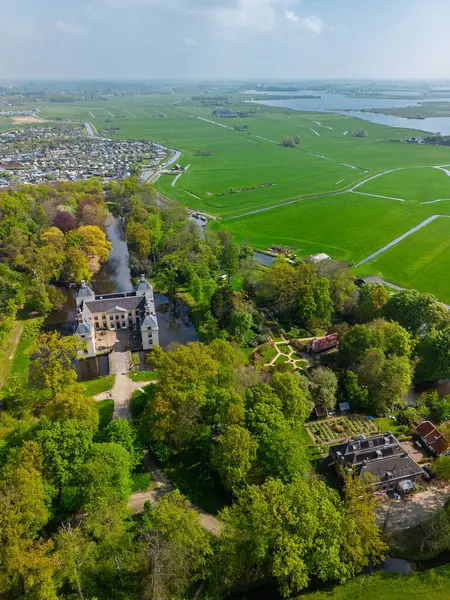 Uçsuz bucaksız yeşil tarlaları, dolambaçlı su yolları ve Hollanda 'nın düz kırsalında parçalı bulutlu bir gökyüzünün altında uzanan bir nehirle çevrili tarihi bir şatonun havadan görünüşü..