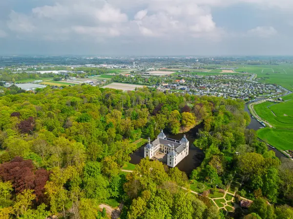 Uçsuz bucaksız yeşil tarlaları, dolambaçlı su yolları ve Hollanda 'nın düz kırsalında parçalı bulutlu bir gökyüzünün altında uzanan bir nehirle çevrili tarihi bir şatonun havadan görünüşü..