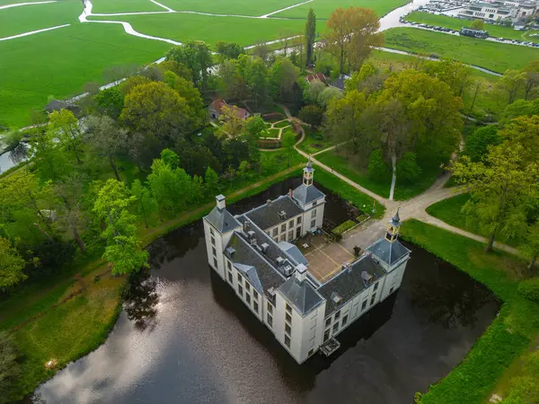 Uçsuz bucaksız yeşil tarlaları, dolambaçlı su yolları ve Hollanda 'nın düz kırsalında parçalı bulutlu bir gökyüzünün altında uzanan bir nehirle çevrili tarihi bir şatonun havadan görünüşü..