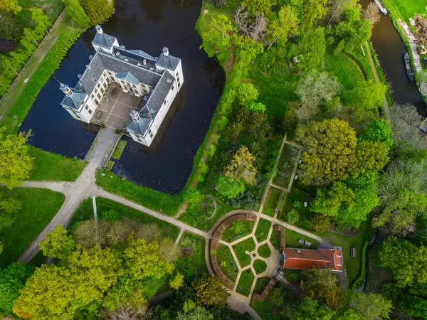 Uçsuz bucaksız yeşil tarlaları, dolambaçlı su yolları ve Hollanda 'nın düz kırsalında parçalı bulutlu bir gökyüzünün altında uzanan bir nehirle çevrili tarihi bir şatonun havadan görünüşü..