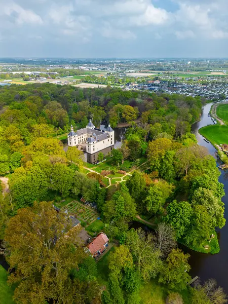 Uçsuz bucaksız yeşil tarlaları, dolambaçlı su yolları ve Hollanda 'nın düz kırsalında parçalı bulutlu bir gökyüzünün altında uzanan bir nehirle çevrili tarihi bir şatonun havadan görünüşü..