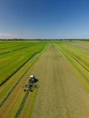Yeşil arazili Hollanda kırsal manzarası, arazide çalışan bir traktör, çiftlik binaları, rüzgar türbinleri, ve modern tarım ve yenilenebilir enerji sergilenen bir kanal..