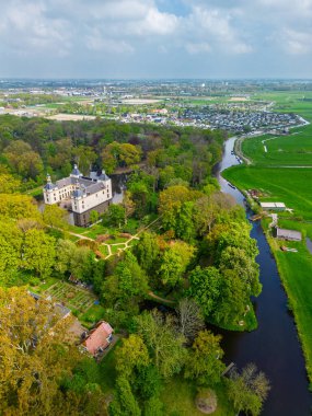 Uçsuz bucaksız yeşil tarlaları, dolambaçlı su yolları ve Hollanda 'nın düz kırsalında parçalı bulutlu bir gökyüzünün altında uzanan bir nehirle çevrili tarihi bir şatonun havadan görünüşü..