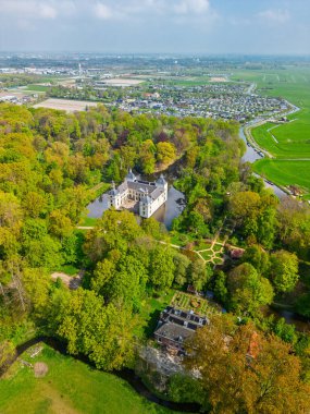 Uçsuz bucaksız yeşil tarlaları, dolambaçlı su yolları ve Hollanda 'nın düz kırsalında parçalı bulutlu bir gökyüzünün altında uzanan bir nehirle çevrili tarihi bir şatonun havadan görünüşü..