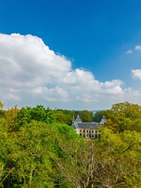 Uçsuz bucaksız yeşil tarlaları, dolambaçlı su yolları ve Hollanda 'nın düz kırsalında parçalı bulutlu bir gökyüzünün altında uzanan bir nehirle çevrili tarihi bir şatonun havadan görünüşü..