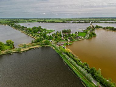 Dar yarımadaları, yeşil tarlaları ve Hollanda kırsalında bulutlu bir gökyüzünün altında sakin sularla çevrili evleri olan manzaralı göl manzaralı bir köy..