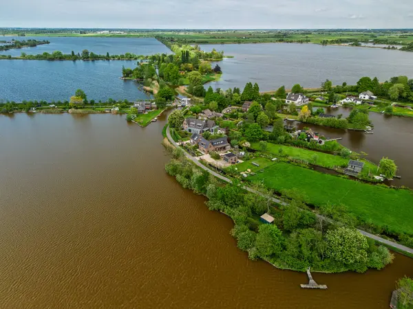 Dar yarımadaları, yeşil tarlaları ve Hollanda kırsalında bulutlu bir gökyüzünün altında sakin sularla çevrili evleri olan manzaralı göl manzaralı bir köy..
