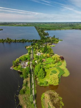 Dar yarımadaları, yeşil tarlaları ve Hollanda kırsalında bulutlu bir gökyüzünün altında sakin sularla çevrili evleri olan manzaralı göl manzaralı bir köy..