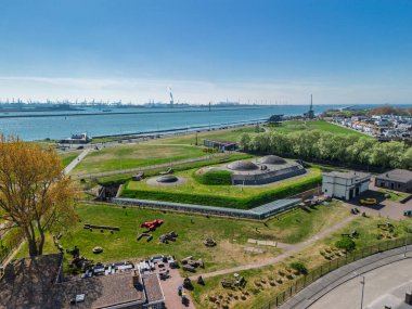 Sığınakları, çimenli manzarası ve geniş nehir, kanal, sanayi limanı ve açık mavi gökyüzü altında vinçleri olan tarihi kıyı kalesinin havadan görünüşü..