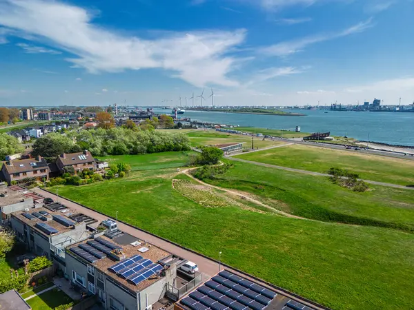 Yeşil parkları, yerleşim alanları, nehir yolu ve işlek nakliye yolları olan bir sahil kasabasının havadan görüntüsü. Rüzgar türbinleri ve endüstriyel liman tesisleri su üzerinde görülebilir..