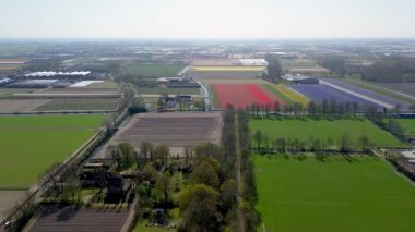 Spor sahalarının havadan görünüşü, koşu pisti, otoparklar ve ağaçlarla çevrili bir otoyol ve açık bir günde ufka uzanan renkli çiçek tarlaları..