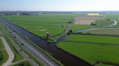 Geleneksel bir yel değirmeni olan, kanal, yeşil tarlalar ve açık mavi gökyüzü altında hareket eden arabaların olduğu bir yol. Renkli bir çiçek tarlasının yukarıdan aşağıya havadan görünüşü.