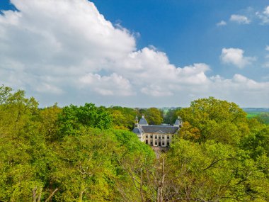 Uçsuz bucaksız yeşil tarlaları, dolambaçlı su yolları ve Hollanda 'nın düz kırsalında parçalı bulutlu bir gökyüzünün altında uzanan bir nehirle çevrili tarihi bir şatonun havadan görünüşü..
