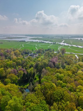 Uçsuz bucaksız yeşil tarlaları, dolambaçlı su yolları ve Hollanda 'nın düz kırsalında parçalı bulutlu bir gökyüzünün altında uzanan bir nehirle çevrili tarihi bir şatonun havadan görünüşü..