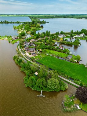 Dar yarımadaları, yeşil tarlaları ve Hollanda kırsalında bulutlu bir gökyüzünün altında sakin sularla çevrili evleri olan manzaralı göl manzaralı bir köy..