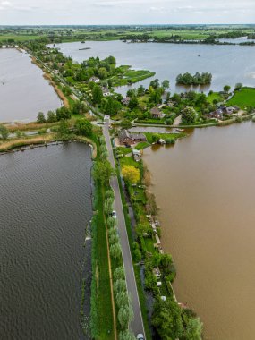 Dar yarımadaları, yeşil tarlaları ve Hollanda kırsalında bulutlu bir gökyüzünün altında sakin sularla çevrili evleri olan manzaralı göl manzaralı bir köy..