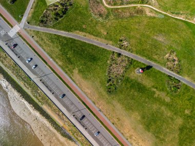 Park etmiş arabaların bulunduğu kıyı yolunun havadan görünüşü yeşil çayırlar boyunca bir patika ve huzurlu bir doğal ortamda küçük bir kırmızı deniz feneri yapısı..