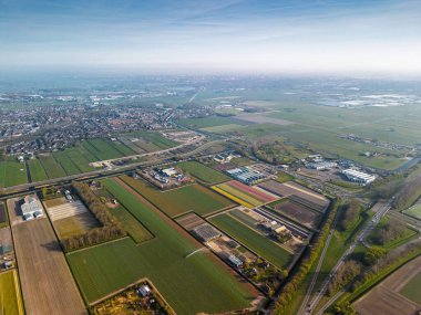Hollanda kırsalının hava panoramik manzarasında tarım arazileri, yeşil tarlalar, ormanlar ve uzak bir kasabaya doğru uzanan bir otoyol var..