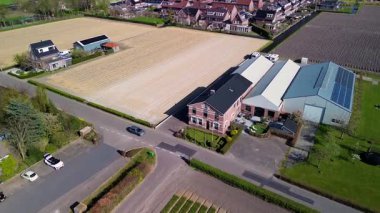 Bir insansız hava aracı temiz tarlaları, konutları, yeşil çimenleri ve güneş panelleri olan binaları olan kırsal bir alanda uçarak huzurlu bir kırsal alan gösteriyor..