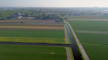 Etrafı tarım arazileri, yeşil ormanlar, bir döner kavşak ve yumuşak güneş ışığı olan açık gökyüzü altındaki uzak kasabalarla çevrili büyük bir bina kompleksi olan kırsal bir bölgenin havadan görünüşü..