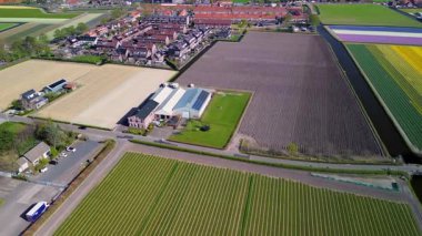 Bir insansız hava aracı temiz tarlaları, konutları, yeşil çimenleri ve güneş panelleri olan binaları olan kırsal bir alanda uçarak huzurlu bir kırsal alan gösteriyor..