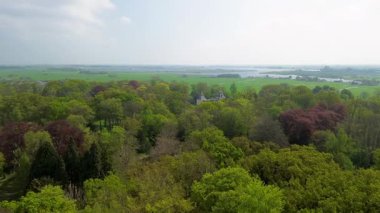 Uçsuz bucaksız yeşil tarlaları, dolambaçlı su yolları ve Hollanda 'nın düz kırsalında parçalı bulutlu bir gökyüzünün altında uzanan bir nehirle çevrili tarihi bir şatonun havadan görünüşü..