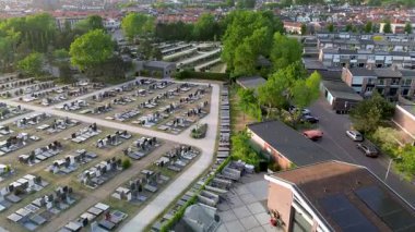 Yuvarlak yolları ve mezar taşlarıyla çevrili, ağaçlarla çevrili ve açık mavi gökyüzünün altındaki yerleşim alanına komşu büyük, düzenli bir mezarlığın havadan görünüşü..