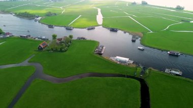 Yeşil tarlaları olan huzurlu bir Hollanda manzarası, yüzen evlerle dolu bir kanal, geleneksel bir yel değirmeni ve bulutlu bir gökyüzünün altında bir marina..
