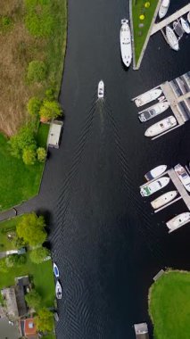 Ahşap rıhtımlar boyunca kenetlenmiş bir marina manzarası, yeşil parklar ve doğal otlaklarla çevrili dar bir su yolunda seyreden bir tekne..