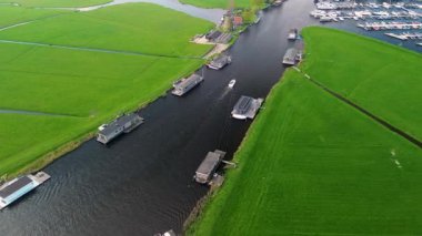 Yeşil tarlaları olan huzurlu bir Hollanda manzarası, yüzen evlerle dolu bir kanal, geleneksel bir yel değirmeni ve bulutlu bir gökyüzünün altında bir marina..