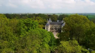 Uçsuz bucaksız yeşil tarlaları, dolambaçlı su yolları ve Hollanda 'nın düz kırsalında parçalı bulutlu bir gökyüzünün altında uzanan bir nehirle çevrili tarihi bir şatonun havadan görünüşü..