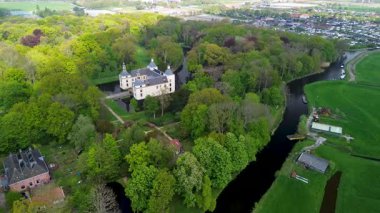 Uçsuz bucaksız yeşil tarlaları, dolambaçlı su yolları ve Hollanda 'nın düz kırsalında parçalı bulutlu bir gökyüzünün altında uzanan bir nehirle çevrili tarihi bir şatonun havadan görünüşü..