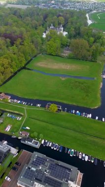 Uçsuz bucaksız yeşil tarlaları, dolambaçlı su yolları ve Hollanda 'nın düz kırsalında parçalı bulutlu bir gökyüzünün altında uzanan bir nehirle çevrili tarihi bir şatonun havadan görünüşü..