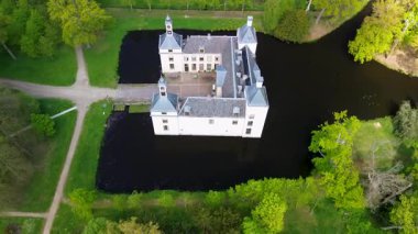 Uçsuz bucaksız yeşil tarlaları, dolambaçlı su yolları ve Hollanda 'nın düz kırsalında parçalı bulutlu bir gökyüzünün altında uzanan bir nehirle çevrili tarihi bir şatonun havadan görünüşü..