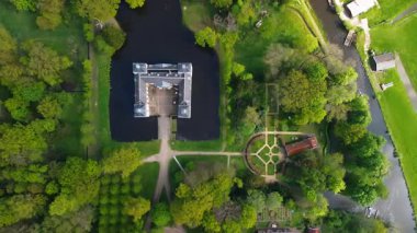 Uçsuz bucaksız yeşil tarlaları, dolambaçlı su yolları ve Hollanda 'nın düz kırsalında parçalı bulutlu bir gökyüzünün altında uzanan bir nehirle çevrili tarihi bir şatonun havadan görünüşü..