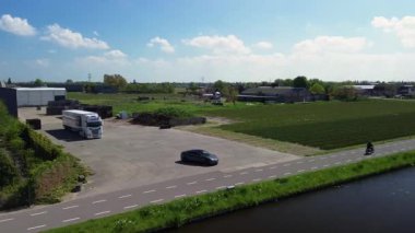 Renkli bir lale tarlasının çiçeklerin arasında yürüyen insansız hava aracı görüntüsü. Siyah bir araba, güneşli bir bahar gününde bir kanal ve modern bir evin yanında kırsal bir yol boyunca sürer..