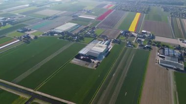 Bir insansız hava aracı temiz tarlaları, konutları, yeşil çimenleri ve güneş panelleri olan binaları olan kırsal bir alanda uçarak huzurlu bir kırsal alan gösteriyor..