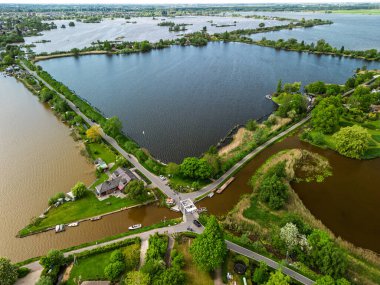 Dar yarımadaları, yeşil tarlaları ve Hollanda kırsalında bulutlu bir gökyüzünün altında sakin sularla çevrili evleri olan manzaralı göl manzaralı bir köy..