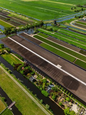 Yeşil tarlaları, kanalları ve geleneksel yel değirmeniyle Hollanda 'nın hava manzarası. Düzgünce bölünmüş araziler ve canlı bitki örtüsü kırsal tarım manzarasının güzelliğini vurguluyor.