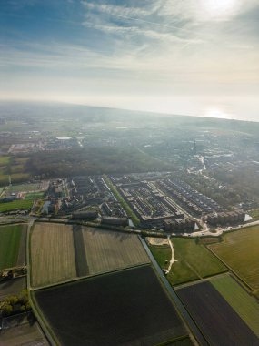 Ufukta Kuzey Denizi parıldarken, Hollanda 'nın tarım arazisine dönüşen puslu hava manzarası. Yumuşak sabah ışığı altında kentsel konutlar, tarlalar ve ormanın karışımı..