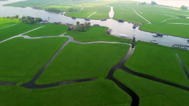 Yeşil tarlaları olan huzurlu bir Hollanda manzarası, yüzen evlerle dolu bir kanal, geleneksel bir yel değirmeni ve bulutlu bir gökyüzünün altında bir marina..