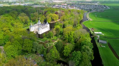 Uçsuz bucaksız yeşil tarlaları, dolambaçlı su yolları ve Hollanda 'nın düz kırsalında parçalı bulutlu bir gökyüzünün altında uzanan bir nehirle çevrili tarihi bir şatonun havadan görünüşü..