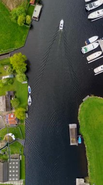 Ahşap rıhtımlar boyunca kenetlenmiş bir marina manzarası, yeşil parklar ve doğal otlaklarla çevrili dar bir su yolunda seyreden bir tekne..