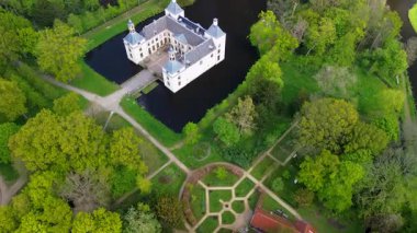 Uçsuz bucaksız yeşil tarlaları, dolambaçlı su yolları ve Hollanda 'nın düz kırsalında parçalı bulutlu bir gökyüzünün altında uzanan bir nehirle çevrili tarihi bir şatonun havadan görünüşü..