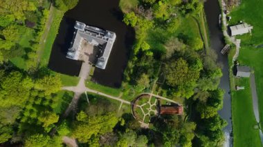 Uçsuz bucaksız yeşil tarlaları, dolambaçlı su yolları ve Hollanda 'nın düz kırsalında parçalı bulutlu bir gökyüzünün altında uzanan bir nehirle çevrili tarihi bir şatonun havadan görünüşü..