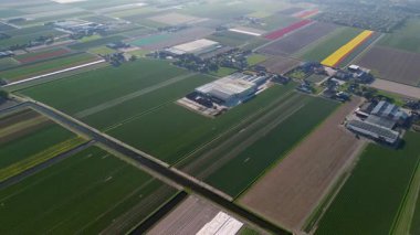 Bir insansız hava aracı temiz tarlaları, konutları, yeşil çimenleri ve güneş panelleri olan binaları olan kırsal bir alanda uçarak huzurlu bir kırsal alan gösteriyor..