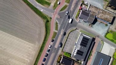 Renkli bir lale tarlasının çiçeklerin arasında yürüyen insansız hava aracı görüntüsü. Siyah bir araba, güneşli bir bahar gününde bir kanal ve modern bir evin yanında kırsal bir yol boyunca sürer..
