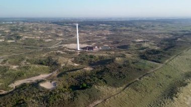 Kum tepeleri ve açık mavi gökyüzü ve sakin deniz ile çevrili sahil boyunca uzanan ve sakin doğal atmosfer yaratan çarpıcı bir kumlu sahil manzarası. Uzun iletişim kulesi