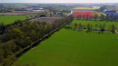 Bir insansız hava aracı temiz tarlaları, konutları, yeşil çimenleri ve güneş panelleri olan binaları olan kırsal bir alanda uçarak huzurlu bir kırsal alan gösteriyor..